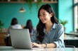 © Maryna - Asian woman sits happily at laptop in modern office. Works with focused expression. Turquoise walls, natural light visible. Interior setting comfortable, tech-savvy. Positive, productive work