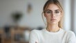 © BROPRADANA - Young businesswoman wearing glasses and a white sweater looks confidently at the camera in a bright modern office.