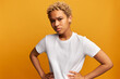 © Anatoliy Karlyuk - Pretty african american gen z girl with blonde curls in white mockup t-shirt holding hands on waist and looking at camera with mistrust, being suspicion on her boyfriend's loyalty isolated on yellow