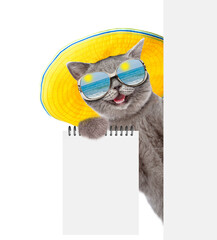 Poster - Happy cat wearing summer hat and sunglasses looks from behind blank white board and showing blank notepad. isolated on white background. Empty space for text