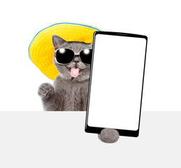 Aufkleber - Happy cat wearing  sunglasses and summer hat looks above blank white board with tongue out and showing big smartphone with white blank screen. isolated on white background. Empty space for text