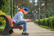 © DimaBerlin - Pensive hipster guy in colorful trendy outfit having come to sunny park for romantic date, sitting on bench, waiting for girlfriend, messaging in smartphone, surfing in internet to spend spare time