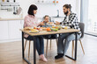 © sofiko14 - Caucasian family with parents and daughter having pizza breakfast in cozy home kitchen setting, sharing meals and bonding.