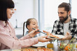 © sofiko14 - Caucasian family having breakfast with pizza and salad. Young parents with daughter sharing meal. Bright kitchen setting, creating joyful and warm family atmosphere.