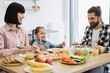 © sofiko14 - Caucasian family with young daughter enjoying breakfast together. Parents and child smiling, eating pizza and fresh salad. Bright morning scene with healthy fruits and orange juice.
