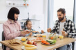 © sofiko14 - Caucasian family, including parents and child, having breakfast with pizza, orange juice, and fresh fruits, creating a joyful atmosphere in a modern, bright kitchen setting.