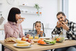 © sofiko14 - Caucasian family of three having breakfast at kitchen table. Adults and child enjoying pizza with orange juice. Relaxed morning scene.