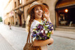 © maxbelchenko - Beautiful young woman in summer style outfit smiling happy walking with flowers in city street.  Fashion style.