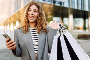 Wall Mural - Happy woman using smartphone while enjoying a day shopping. Black Friday, sale and discount. Buying clothes presents for holidays.