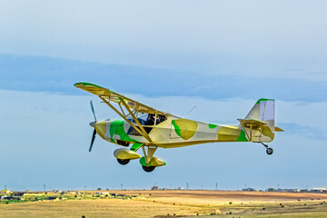 Small two-seater single engine home built kit plane with camouflage paint scheme taking off from small airfield in the Western Cape, South Africa