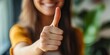 © StockKing - Smiling woman with long hair giving a thumbs up gesture in a bright indoor setting with green plants blurred in the background, warm tones predominant.