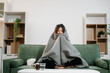 © Nuttapong punna - Young Asian woman suffering from flu symptoms, covered with a blanket on a sofa. Concept of illness, healthcare,