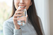 © KMPZZZ - Happy beautiful, asian young woman, girl drinking, sip fresh glass of water for hydration of body, holding transparent glass in her hand, thirsty at home. Health care, healthy lifestyle concept.