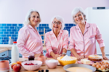 Wall Mural - Beautiful senior women having funny pajama party at home - Group of cheerful elderly female friends having fun at home and baking in the kitchen, concepts about old people, lifestyle, quality of life