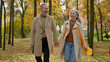 © Yuliia - Happy old senior married couple adults hold hands together walking in city park joyful mature gray haired Caucasian woman wife and man husband have fun talking laughing walk stroll in autumn forest