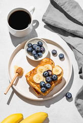 Wall Mural - Peanut butter toast  with banana and blueberry on a plate on a light background