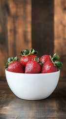 Wall Mural - Freshly picked strawberries arranged in a white bowl against a rustic wooden background during daylight hours