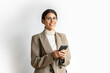 © Stock 4 You - Smiling young middle eastern businesswoman using smartphone mobile phone online ai app for work isolated on white background. Woman it specialist in business suit holding cellphone. Portrait at camera