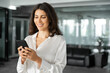 © Stock 4 You - Portrait it specialist business woman manager ceo using cell phone mobile ai application for online work. Focused Latin Hispanic female businesswoman holding smartphone standing in office. Copy space