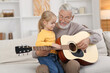© New Africa - Grandpa teaching his granddaughter to play guitar on sofa at home