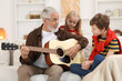 © New Africa - Grandpa playing guitar for his grandkids on sofa at home