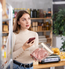 Wall Mural - Young female shopper scanning qr code for packaged raw pork meat in grocery store