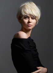 Poster - Elegant young woman with short blonde hair posing confidently against a neutral gray background. Fashion and beauty concept with a soft expression.