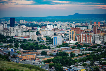 Krasnoyarsk, russia, city skyline featuring residential and industrial buildings at sunset with a mountain in the background