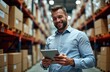 © Pete - Happy salesman in warehouse checks supplies on tablet. Man in light blue shirt works in large hardware store. Stands amidst storage racks filled with boxes. Seems satisfied with job. Uses technology