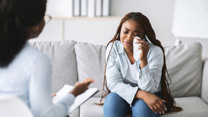 Wall Mural - Unhappy black female client consulting psychologist, crying at medical office, banner design. Psychiatrist helping depressed African American woman with nervous breakdown at mental health clinic