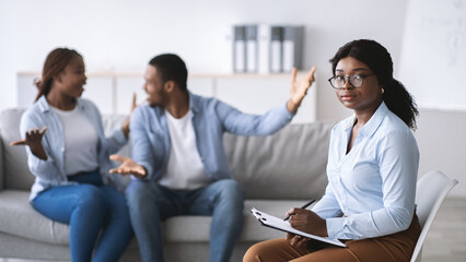 Wall Mural - Unhappy female psychologist and black married couple having fight during session at office, copy space. Marital counseling, psychotherapy of divorces and relationship problems concept