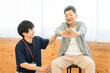 © buritora - リハビリで体操をするシニア男性と理学療法士・作業療法士の男性スタッフ
