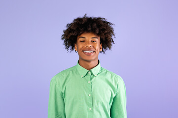 Casual teenage model. Portrait of smiling african american guy in braces looking at camera, wearing mint shirt, posing isolated over blue background, studio shot