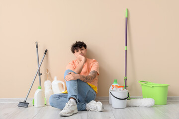 Wall Mural - Upset young man with cleaning supplies sitting near beige wall