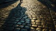 © Suphawan - Shadows of a person holding an umbrella stretching across a cobblestone street in the morning sun