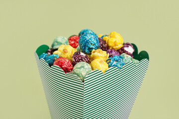 Wall Mural - Bucket with sweet colorful popcorn on green background, closeup