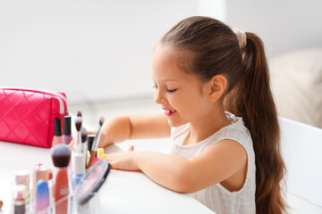 Wall Mural - Cute little girl with cosmetic bag and different makeup products at table in living room