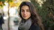 © The 2R Artificiality - Young Greek woman with long brunette hair wearing a gray scarf, posing outdoors in Athens, Greece, surrounded by greenery and autumn colors.