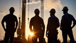 © chatchai - Construction team silhouettes at sunset, showcasing teamwork and dedication. workers wear hard hats and safety gear, standing against backdrop of cranes and machinery