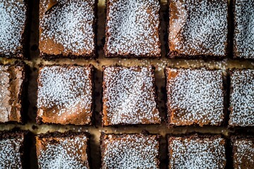 Freshly baked brownies cut into squares, dusted with powdered sugar, on a rustic wooden table