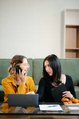 Two women collaborating on a project at home, brainstorming with a laptop and notebook in a cozy setting.