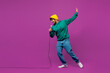 © ViDi Studio - Full body side view young happy Indian man he wear green hoody yellow hat casual clothes sing song in microphone at karaoke club isolated on plain purple background studio portrait. Lifestyle concept.
