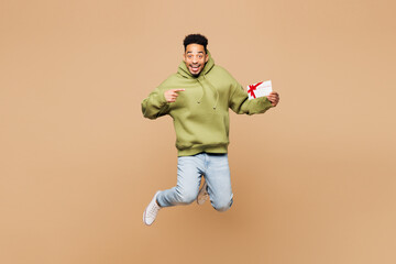 Sticker - Full body young man of African American ethnicity wears green hoodie casual clothes jump high hold point on store gift certificate coupon voucher card isolated on plain pastel light beige background.