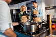 © Zoran Zeremski - Couple enjoying a cooking class with a chef preparing meal in the kitchen, woman recording with smart phone.