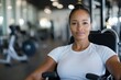 © Milos - A confident woman resting with a satisfied expression while seated on gym equipment, showcasing her strength and commitment to a healthy lifestyle.