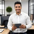 © GEO - Un nuevo empleado hispano en una oficina, sosteniendo una tableta mientras trabaja. Tiene una expresión apasionada y alegre, sonriendo mientras mira la tableta. Lleva una camisa blanca de manga larga.