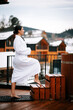 © Darius - Woman in white swimsuit steps into hot water surrounded by winter mountain scenery with wooden structures in background