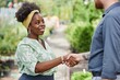 © Seventyfour - Medium shot of cheerful African American female landscape designer shaking hands with male partner making successful business deal while meeting outside in plant nursery, copy space
