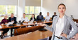 © JackF - Portrait of positive woman secretary standing in meeting room and making presenting gesture during conference with colleagues.