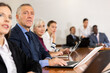 © JackF - Focused mature white business man in formal suit sitting with colleagues in conference room and absorbedly listening to speaker's presentation during corporate group meeting